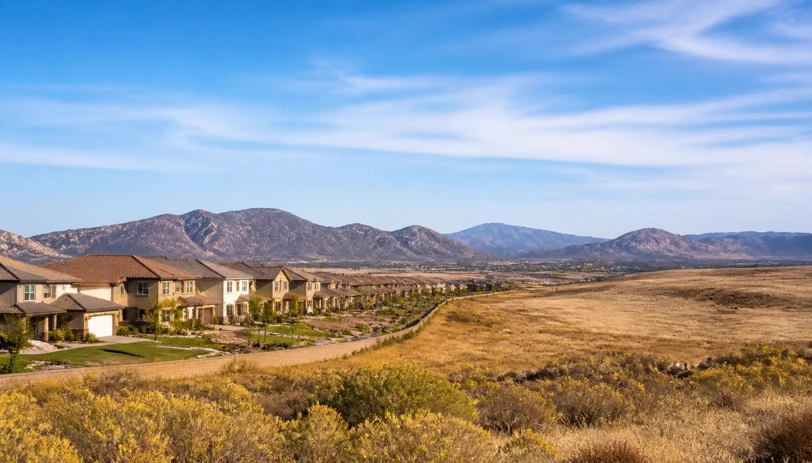 New Menifee, CA tract homes with green lawns bordering open dry grassland and distant mountains