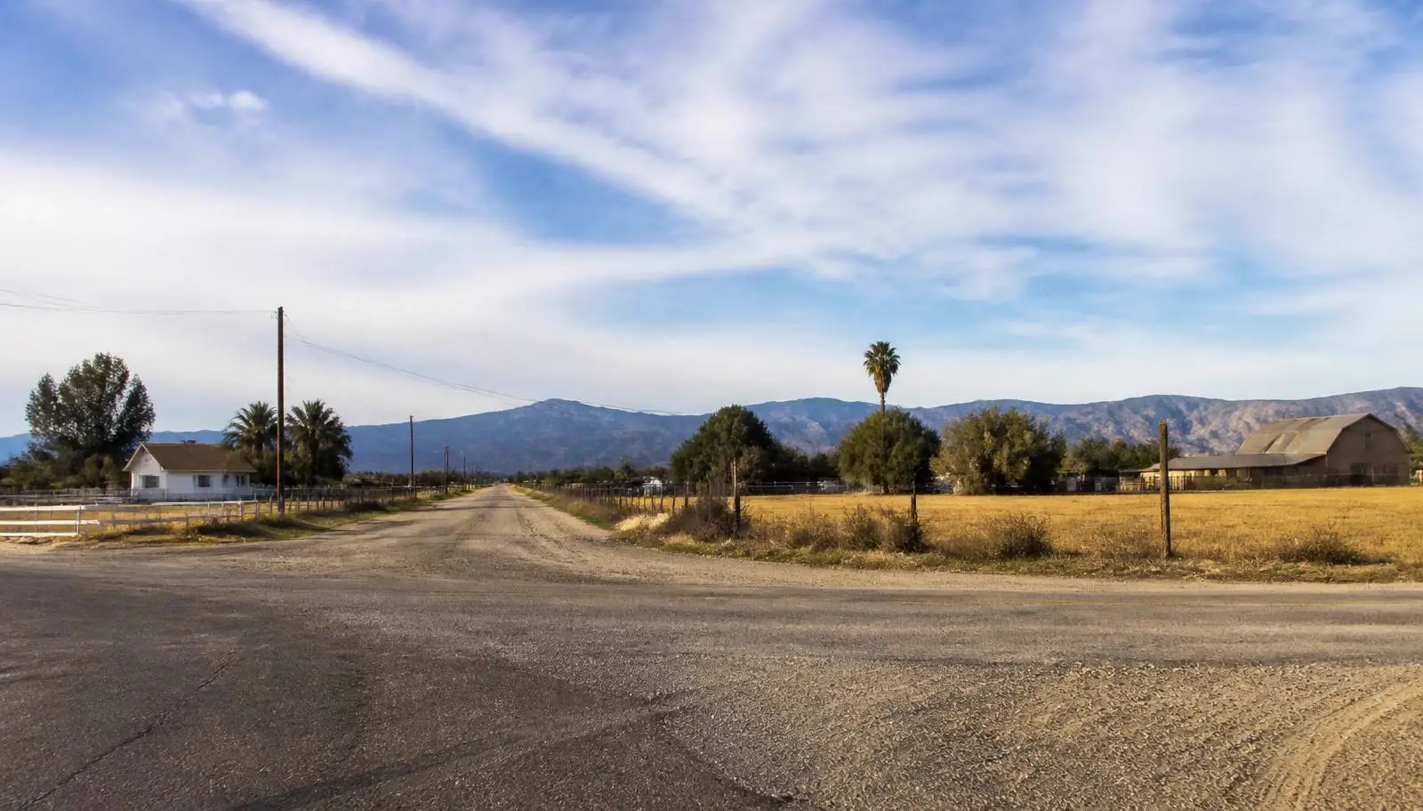 Rural Romoland, CA crossroads with dry open fields, older homes, and distant mountain ridges