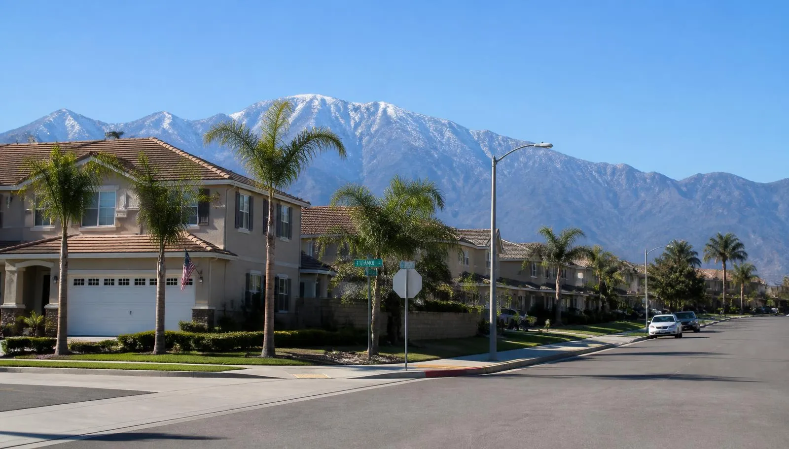 Residential street of tile-roof homes and palm trees in Fontana, CA with the San Gabriel Mountains behind it